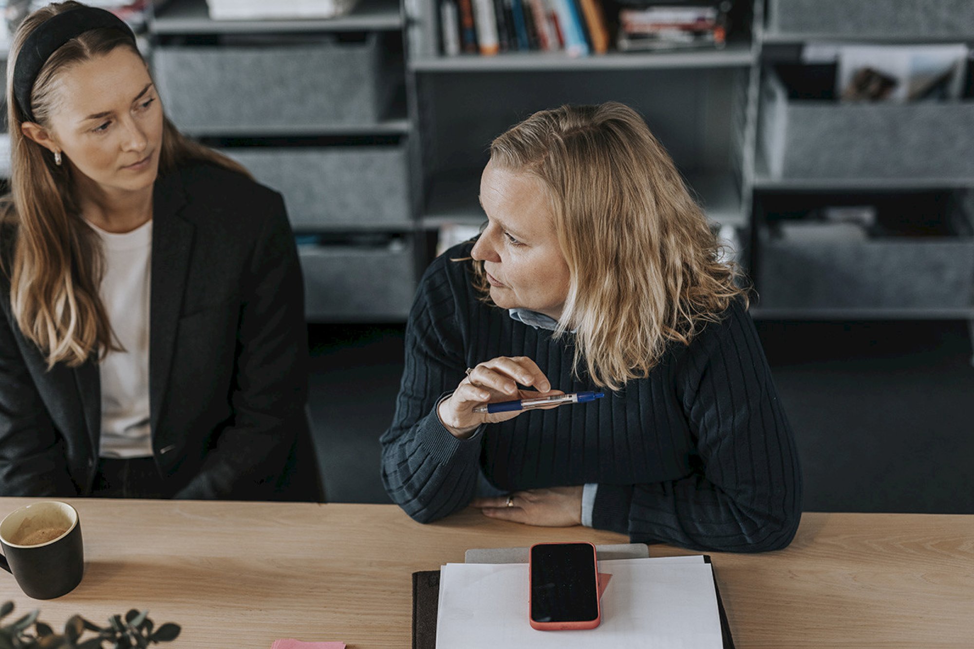 To kvinner sitter på et bibliotek og diskuterer mens de studerer