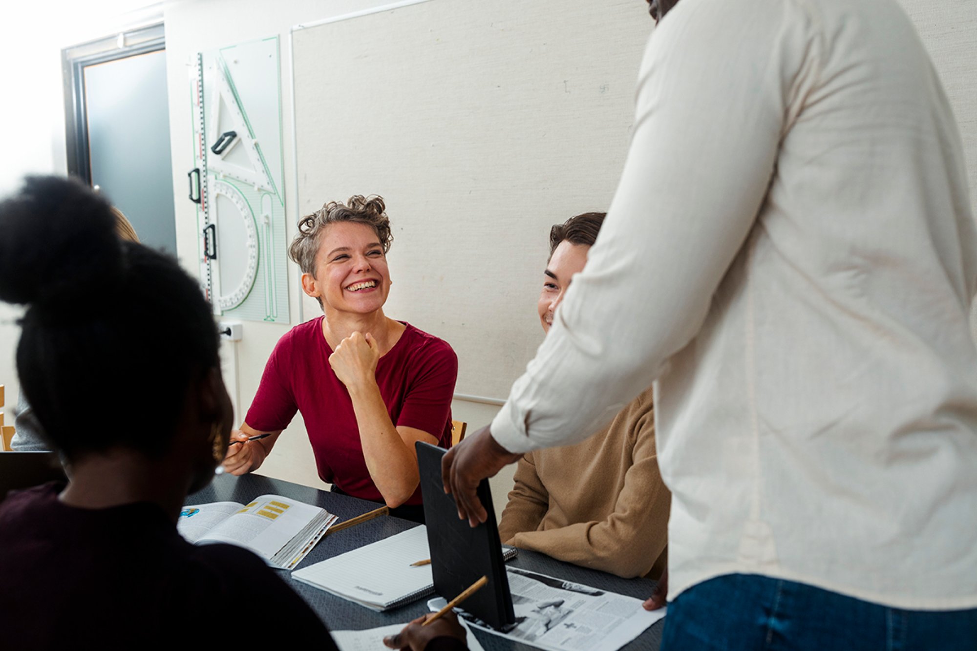 En smilende dame sammen med en gruppe studenter rundt et bord