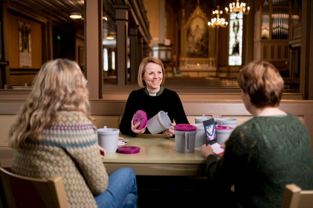 En prest sitter i en kirke og snakker med to personer.