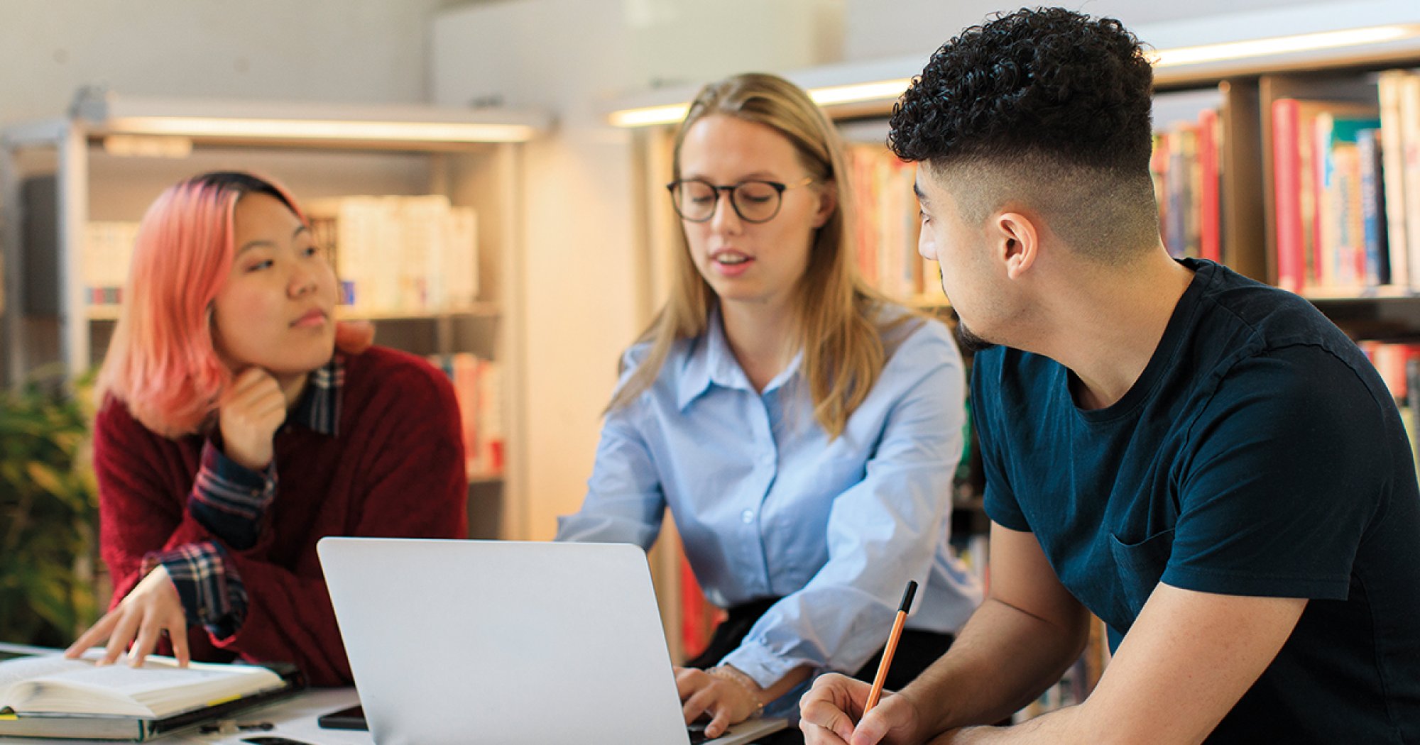 Tre studenter diskuterer og ser på laptop