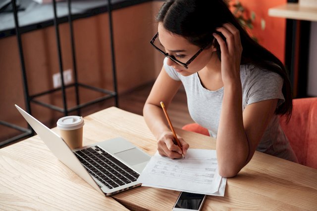 Kvinne med briller og kaffekrus foran PC